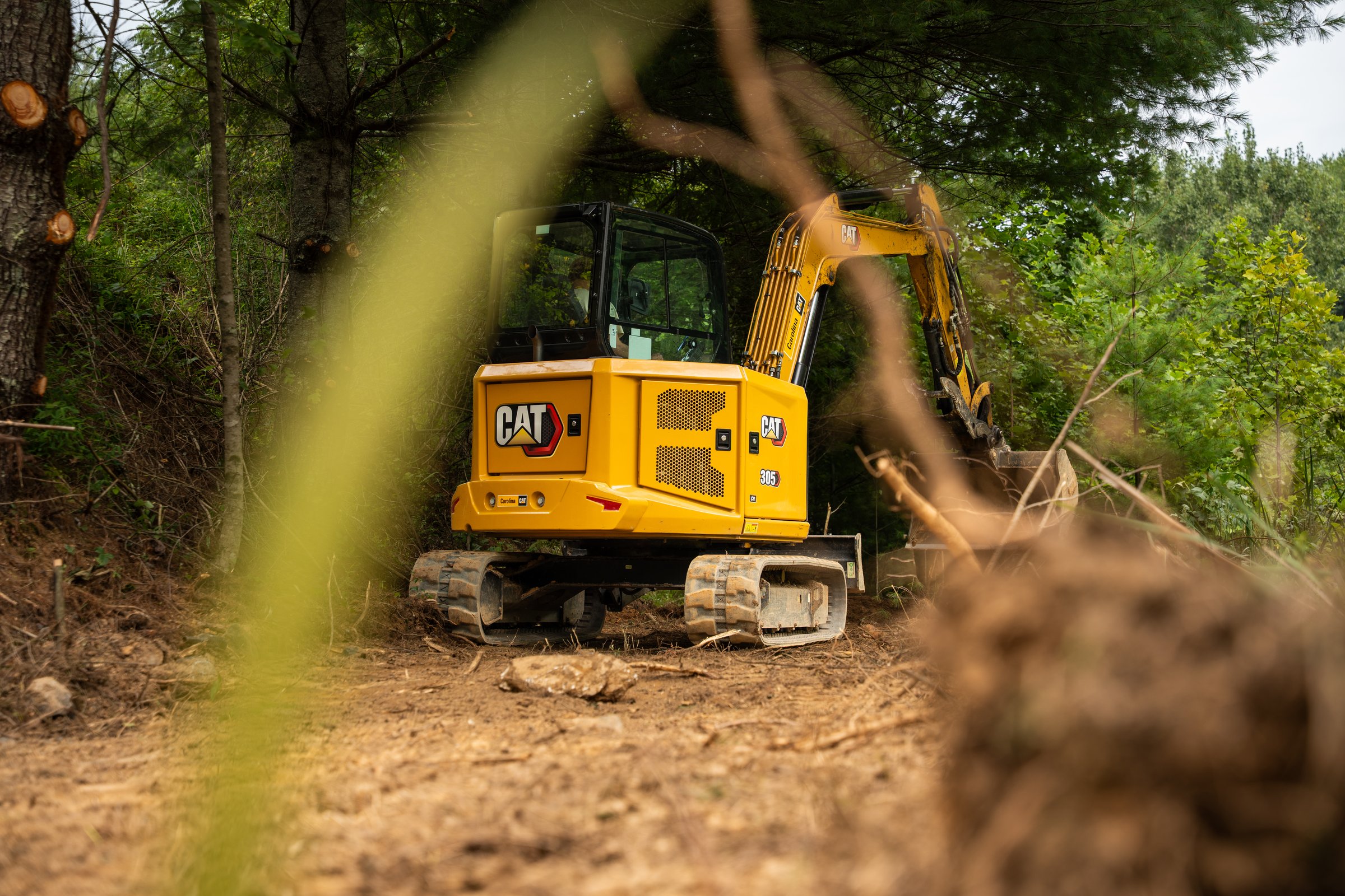 Excavator framed through brush on a cleared trail
